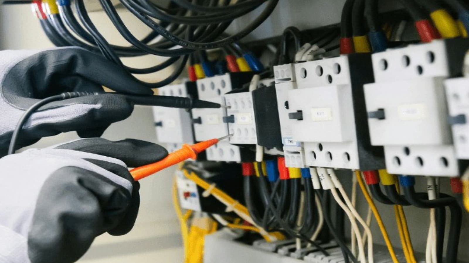Handen met beschermende handschoenen meten een elektrische installatie door
