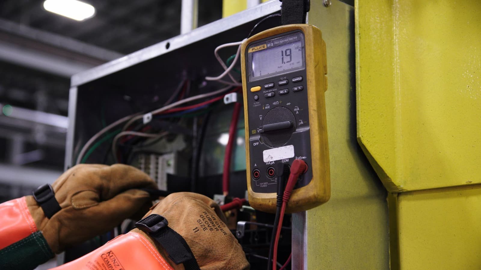 Een monteur met beschermende handschoenen meet met een multimeter in een schakelkast