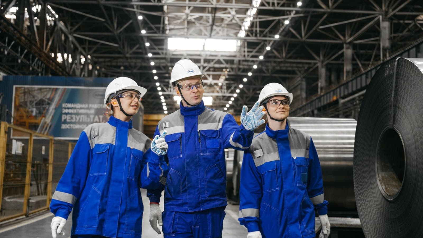 Drie medewerkers met veiligheidshelmen en brillen overleggen in een productiehal