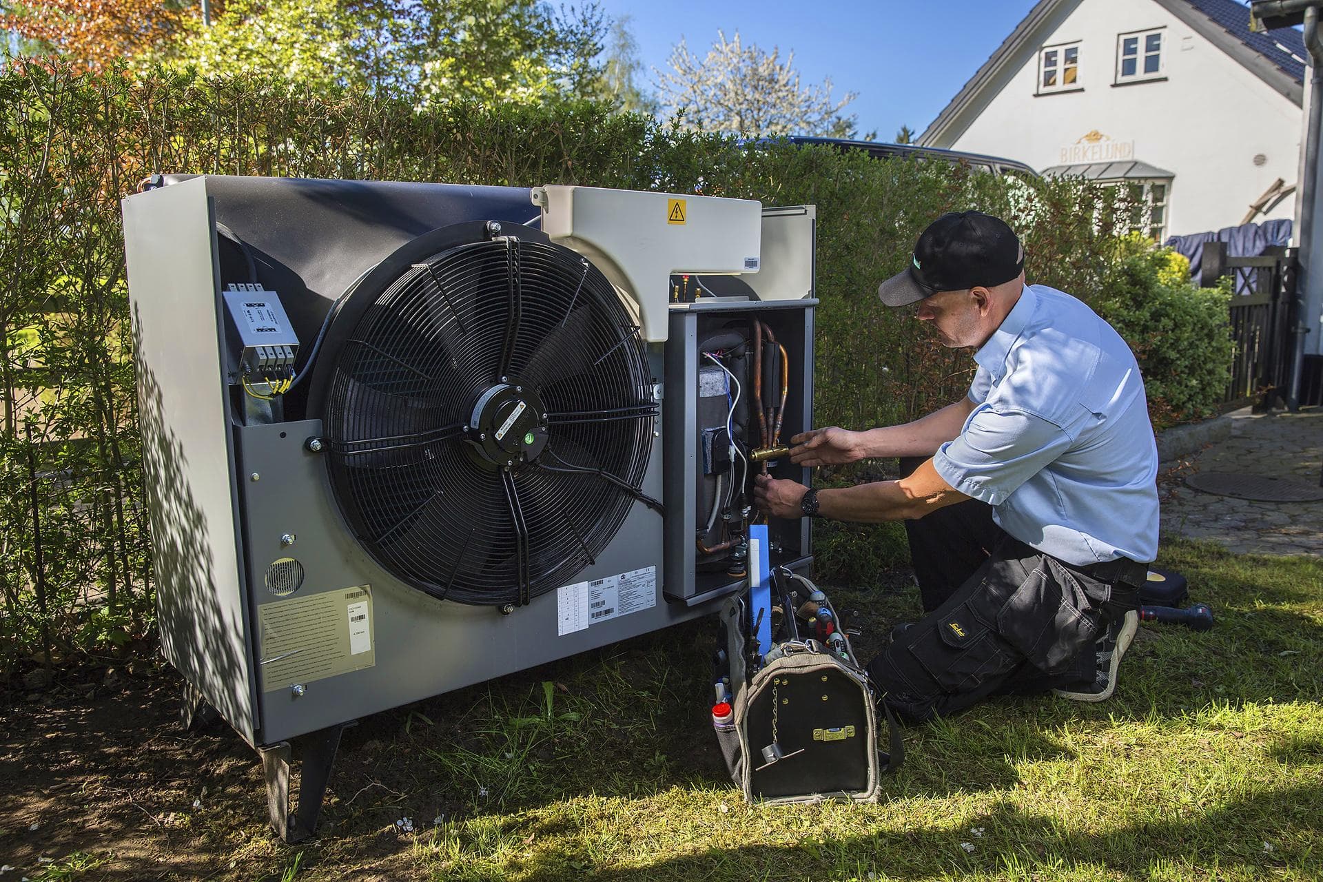 Installatiemonteur werkt aan de aansluitingen van een buitenunit naast een woning