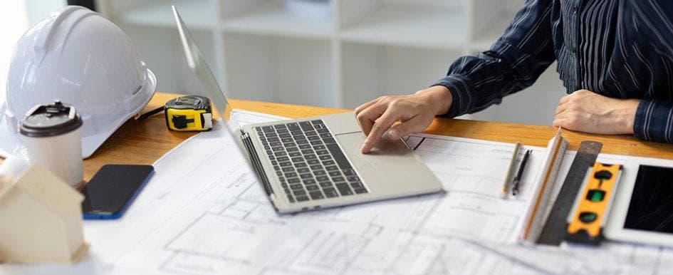 Projectmedewerker maakt een berekening met laptop en bouwtekeningen
