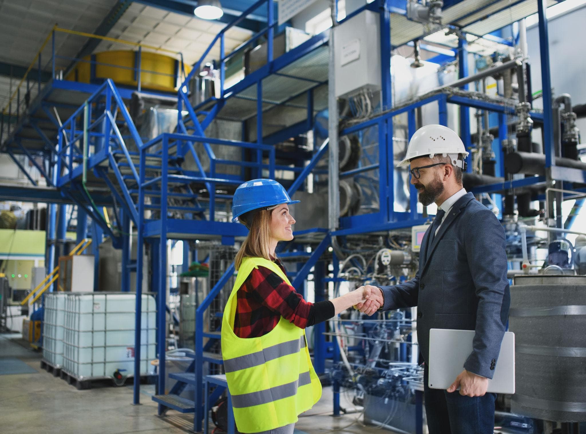 Twee professionals met bouwhelmen schudden handen in een industriële omgeving